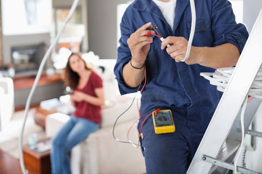 Electrician looking at wires with homeowner sitting on the couch behind him.